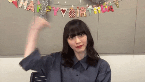 a woman is sitting in front of a wall with a happy birthday banner .