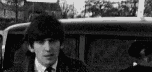 a black and white photo of a young man in a suit and tie sitting in a car .