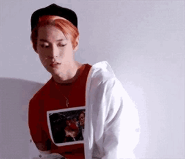 a young man with red hair is wearing a red shirt and a white jacket .