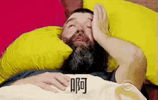 a man with a beard is laying in bed holding his head