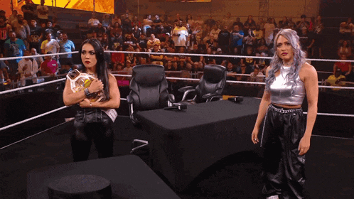 two women are standing in a wrestling ring holding a belt