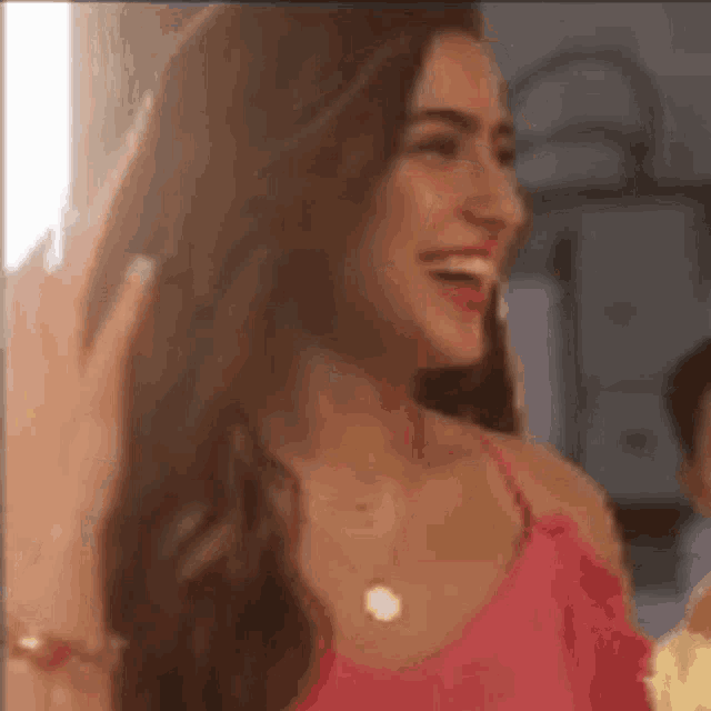 a woman in a pink top is laughing and smiling while standing in a room .