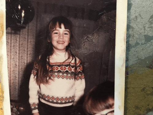 a little girl wearing a sweater with the letter x on it smiles for the camera