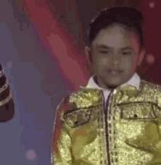 a young boy in a gold jacket is standing in front of a red light .