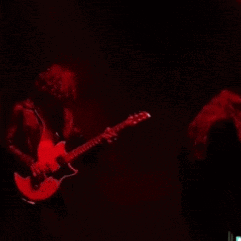 a man in a black jacket is playing a guitar in a dark room .