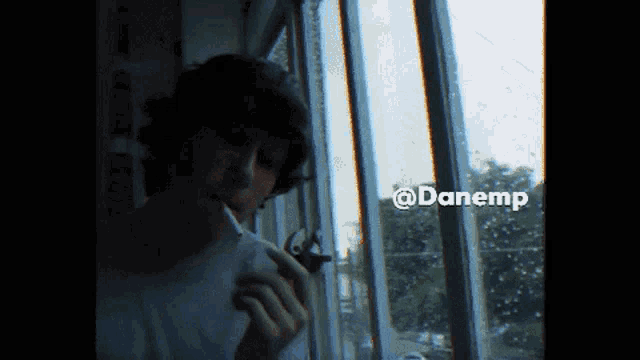 a man is smoking a cigarette in front of a window with the hashtag @danemp on the bottom