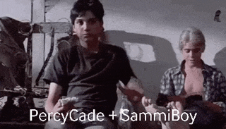 two men are sitting next to each other in a room with the words percycade + sammiboy written on the screen .