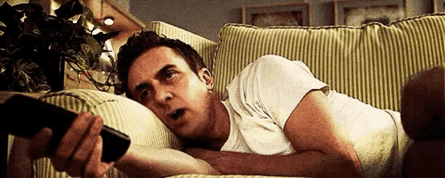 a man laying on a couch with a remote control in his hand