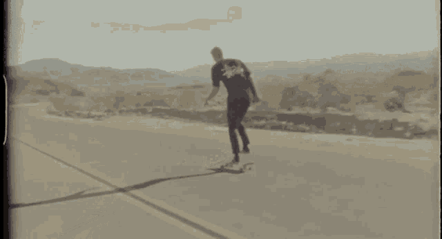 a man in a stussy shirt is riding a skateboard down a road