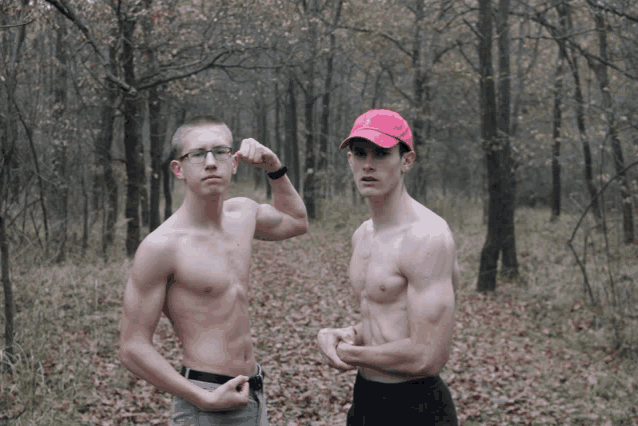 a shirtless man flexes his muscles next to a shirtless man wearing a red hat