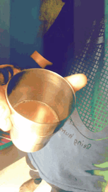 a person is holding a cup of tea in front of a shirt that has the word mun written on it