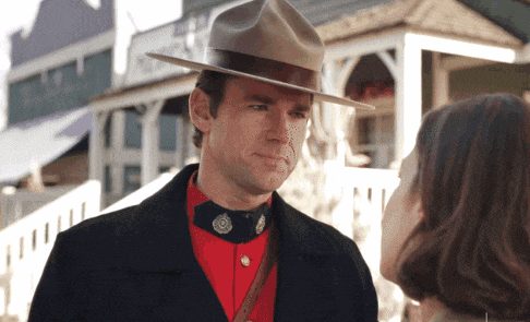 a man wearing a hat and a red shirt looks at a woman