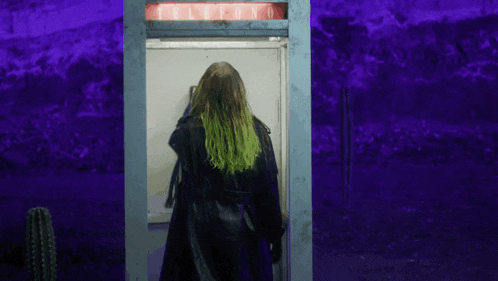 a woman with green hair is standing in a payphone