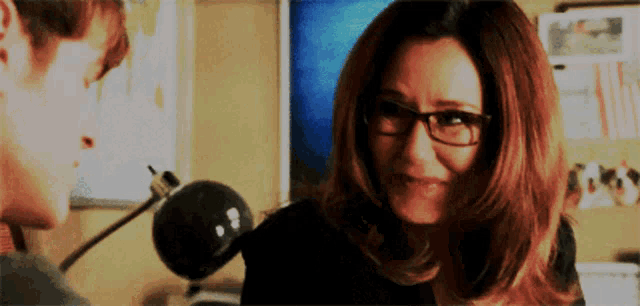 a woman wearing glasses looks at a man in a room