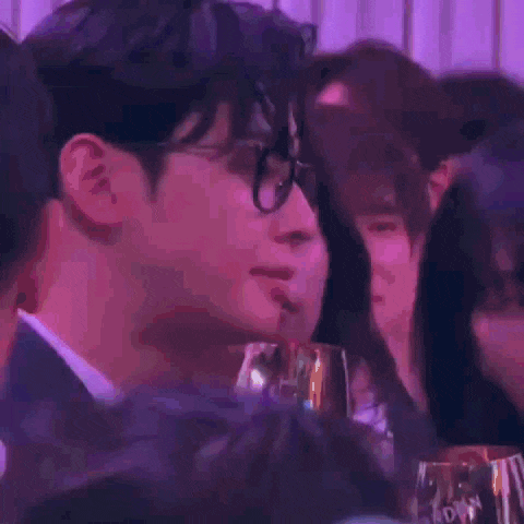 a man in a suit and tie is drinking from a glass while sitting at a table with other people .