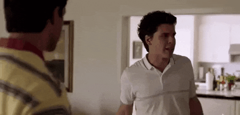 two men are standing next to each other in a living room and talking .