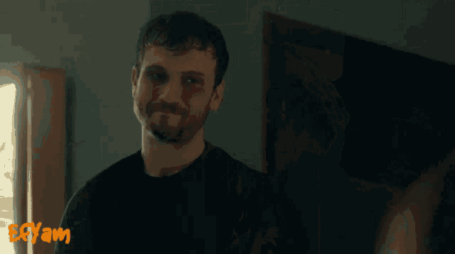 a man in a black shirt is smiling in front of a sign that says eayam