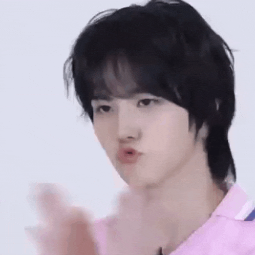 a young man with black hair is wearing a pink shirt and making a face .