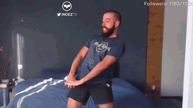 a man in a hard rock shirt is dancing in a bedroom