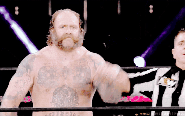 a shirtless wrestler with a tattoo on his chest stands in a ring with a referee wearing an amf shirt