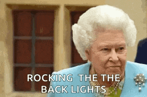 queen elizabeth ii is wearing a blue jacket and pearls and is standing in front of a window .