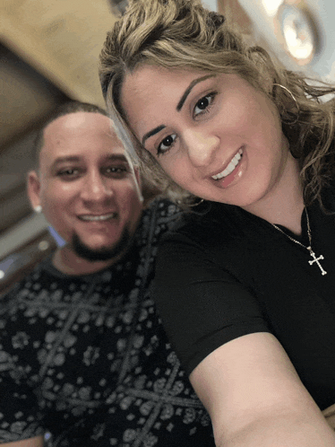 a man and woman are posing for a picture and the woman has a cross necklace