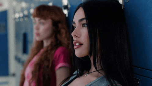two girls are leaning against a blue wall and one has a necklace on her neck