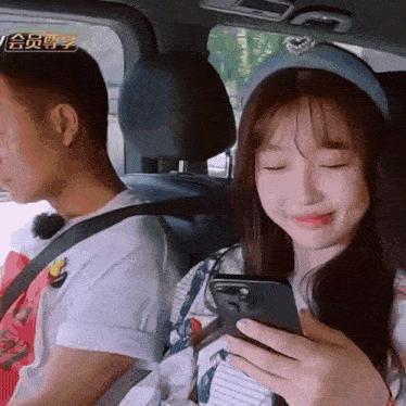 a man and a woman are sitting in a car and the woman is smiling while looking at her phone
