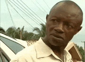 a man in a white shirt is standing in front of a car and making a funny face .