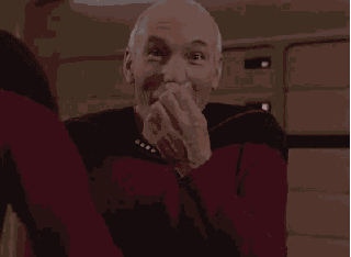 a man in a red sweater is laughing with his hands on his face .