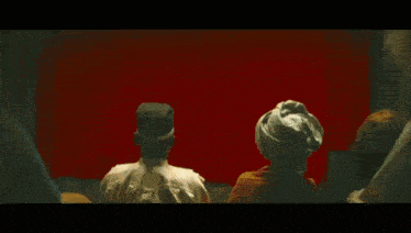 a man in a hat is standing in front of a red curtain looking out a window .
