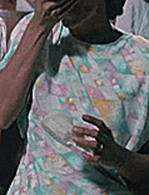 a man in a colorful shirt is talking on a cell phone while holding a glass .