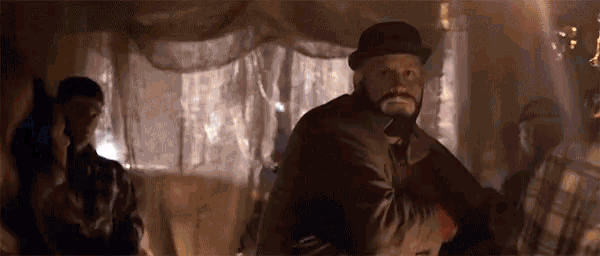 a man with a beard and a hat is standing in a dark room with other people .