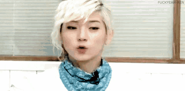 a young man with blonde hair is wearing a blue scarf around his neck and making a funny face .