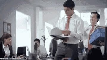a man in a white shirt and red tie is standing in an office holding a folder .