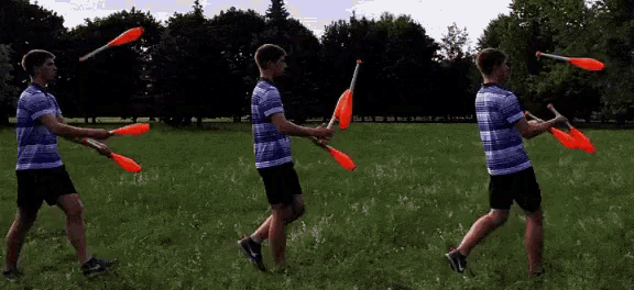 a man in a striped shirt is juggling three orange sticks in a field