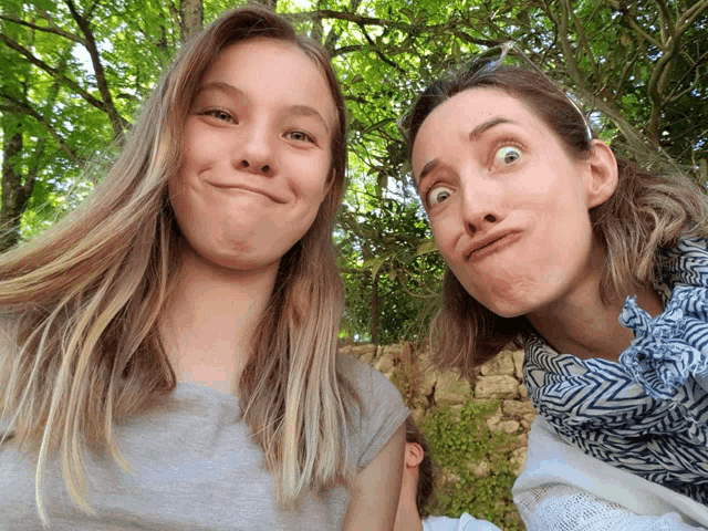 two women are making funny faces in front of a tree