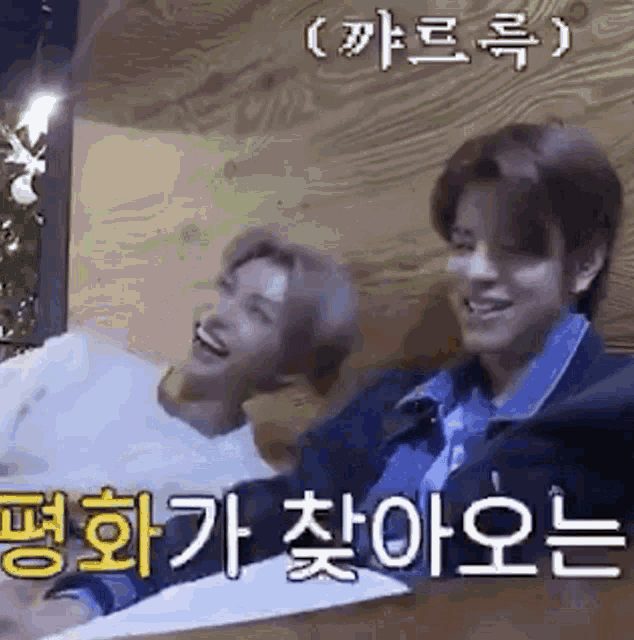 two young men are sitting next to each other on a wooden table and laughing .