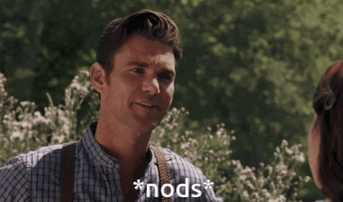 a man in a plaid shirt with suspenders is talking to a woman with the words * nods * above him