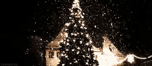 a christmas tree is lit up with snow falling in front of a building