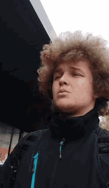 a young man with curly hair wearing a black jacket