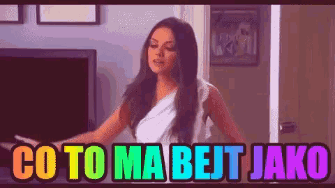 a woman is standing in front of a television with the words co to ma bejt jako written in rainbow colors