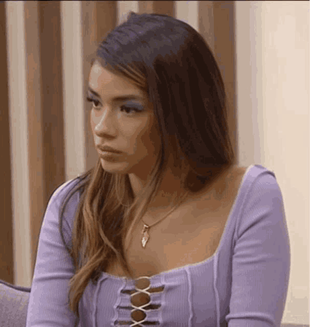 the woman is wearing a purple top and a necklace .