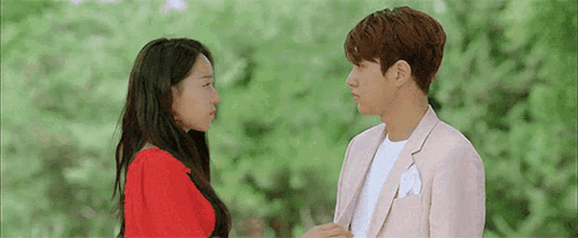 a man in a pink suit and a woman in a red dress are looking at each other in a park .