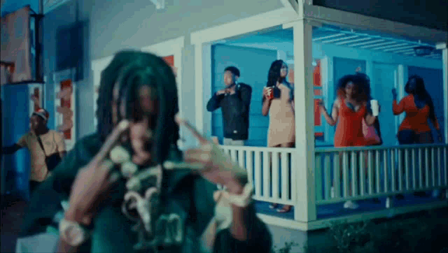 a man with dreadlocks is standing on a porch with a group of people standing around him .