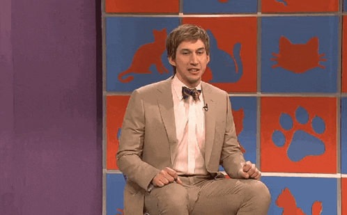 a man in a suit and bow tie is sitting with his arms outstretched in front of a wall with cats on it