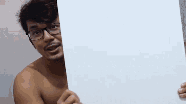 a shirtless man with glasses is holding a white board .