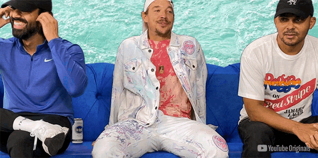 three men are sitting on a blue couch and one of them is wearing a shirt that says pepsi stripe