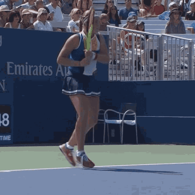 a woman playing tennis in front of an emirates advertisement