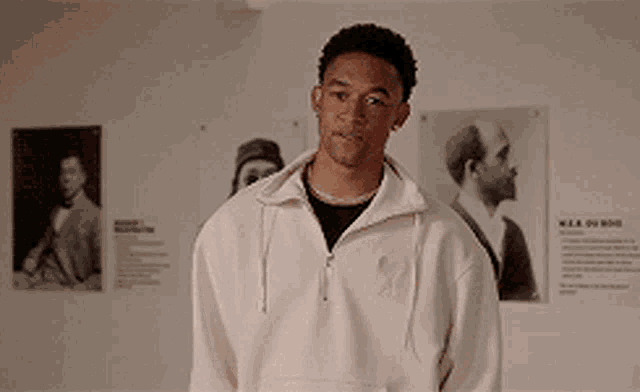 a man wearing a white sweatshirt is standing in front of a wall with pictures on it
